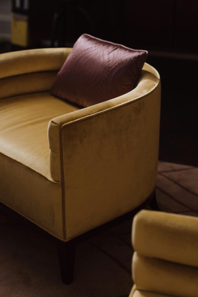 Elegant yellow velvet chair with pink cushion in a cozy, stylish indoor setting.