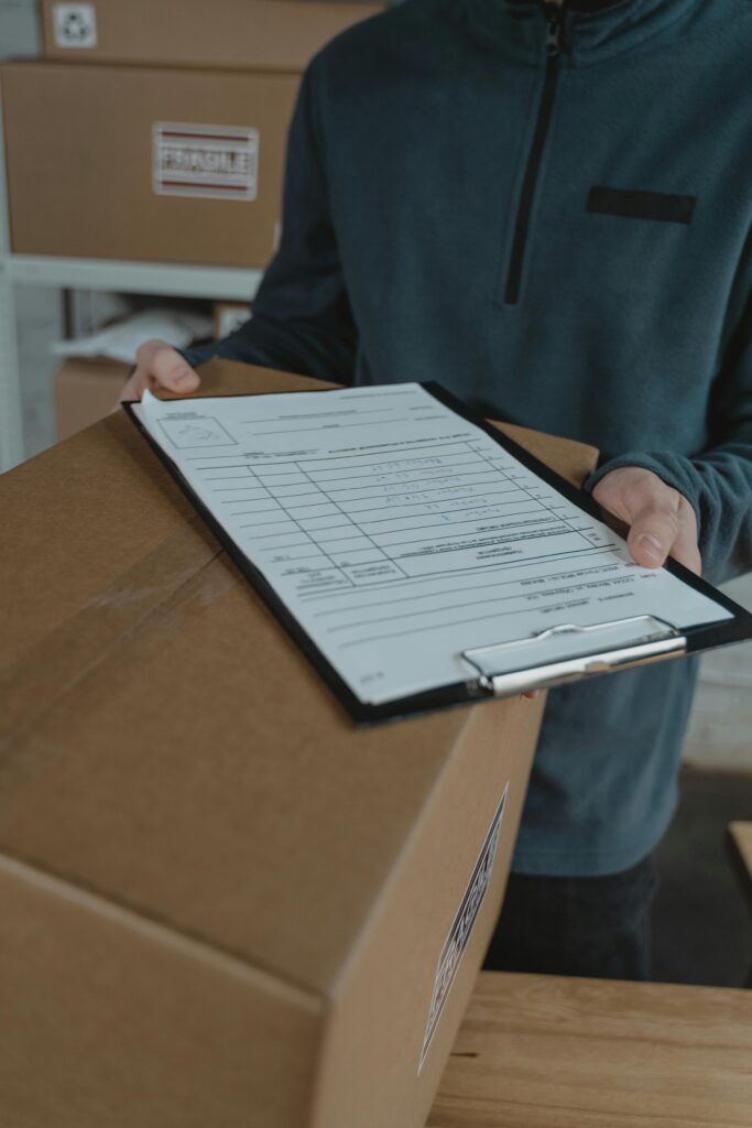 pexels-photo-6170102-6170102 Person in a warehouse holding a box with a shipping checklist on a clipboard.