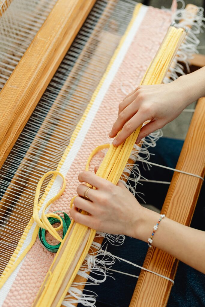 Close-up of hands weaving colorful threads on a traditional wooden loom.