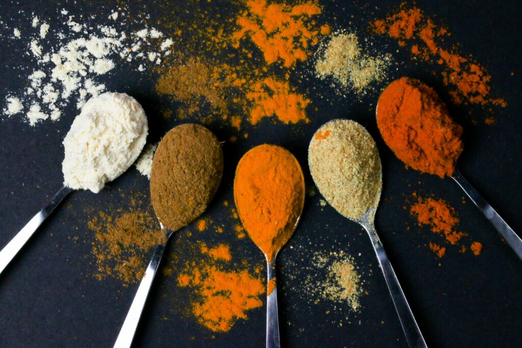 Five spoons of vibrant spices against a black background, showcasing culinary diversity.
