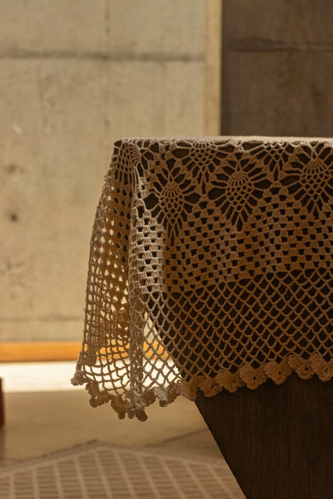 Close-up of a beautifully patterned crochet tablecloth draped over a rustic wooden table.