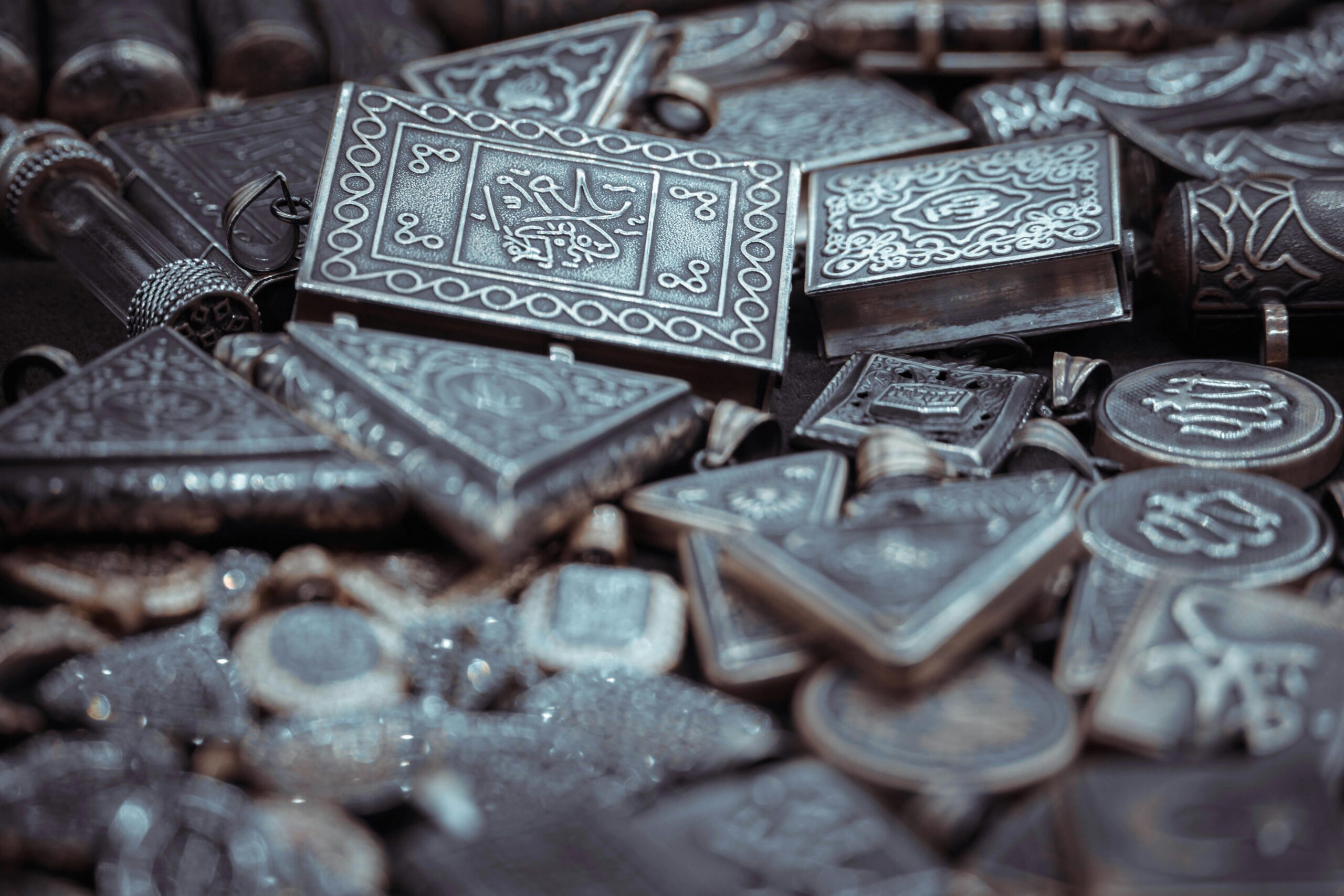 Close-up of antique silver amulets with ornate engravings in selective focus.